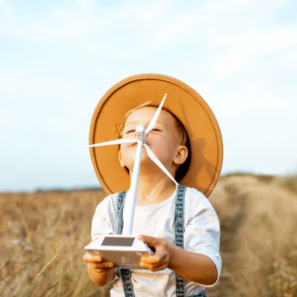 Porträt eines neugierigen Jungen, der auf einem Feld mit einem Spielzeug-Windrad spielt und schon in jungen Jahren erforscht, wie grüne Energie funktioniert.